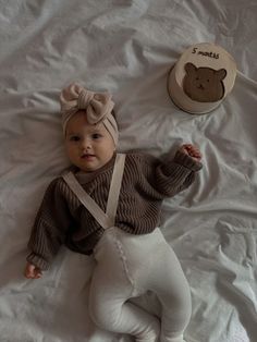 a baby laying on top of a bed next to a teddy bear hat and stuffed animal