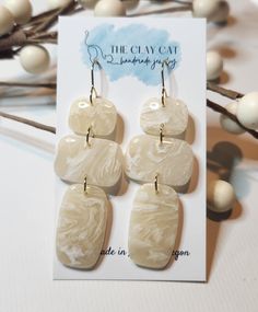 the clay earrings are made in ivory and beige tones, with gold - plated hooks