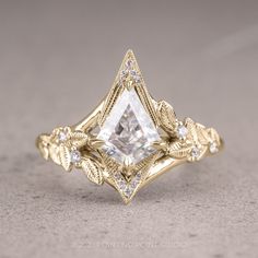 a gold ring with a white diamond in the center and leaves around it, on a gray surface