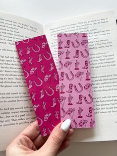 two bookmarks with pink and red designs are held in front of an open book