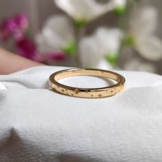 a close up of a gold wedding ring on a white cloth with flowers in the background