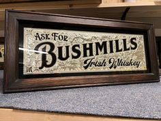 a framed sign that says ask for bushmills fresh whiskey on the side of a shelf