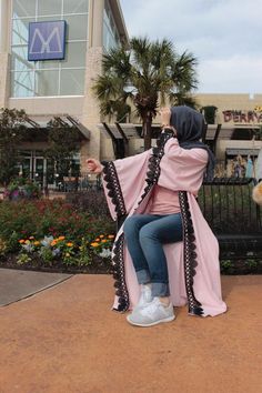 a woman sitting on top of a wooden bench wearing a pink coat and blue jeans