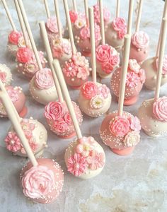 there are many pink and white cake pops on the table, with flowers on them