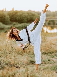 a woman is doing karate in a field with her legs spread out and one leg up