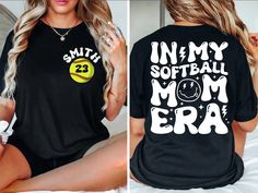 a woman sitting on top of a bed wearing a shirt that says in my softball mom era