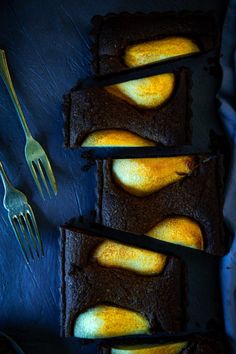 four slices of chocolate cake with pears on top and forks next to it,