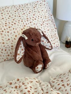 a brown stuffed animal sitting on top of a bed next to pillows and lamp shades