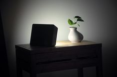 a white vase sitting on top of a wooden table next to a black square object