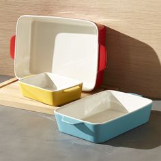 two square dishes sitting next to each other on top of a wooden table, one yellow and the other blue