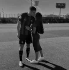 a man and woman standing next to each other on a field with a basketball hoop in the background