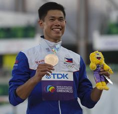 a man holding a stuffed animal in his hand and smiling at the camera while wearing a gold medal