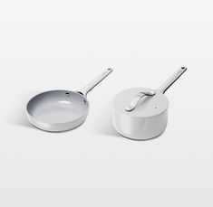 two white pots and pans on a white surface with spoons in the middle