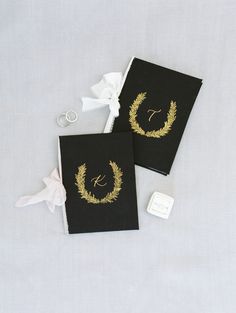 two black wedding guest book with gold monogrammed wreaths and initials on them