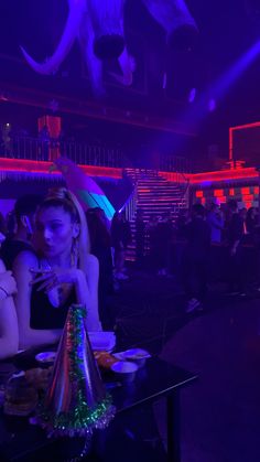 a woman sitting at a table in front of a purple light with an elephant head hanging from the ceiling