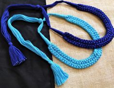 three pieces of blue rope with tassels are laying on a piece of black fabric