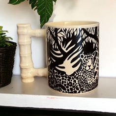 a black and white mug sitting on top of a shelf next to a potted plant