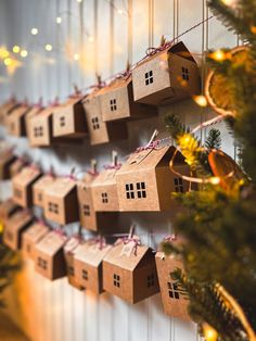 several cardboard houses hanging on a wall with christmas lights in the back ground and small trees behind them