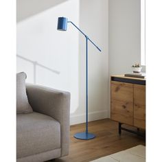 a blue floor lamp next to a couch in a living room with white walls and wooden floors