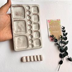 a hand holding a plastic tray next to a flower and some other items on a table