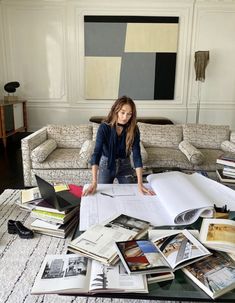 a woman sitting on top of a couch surrounded by books and papers in a living room