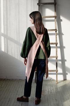 a woman standing in front of a ladder wearing a green shirt and pink scarf over her shoulders