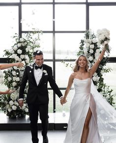 a bride and groom walking down the aisle with their arms in the air holding hands