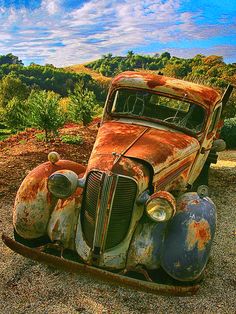 an old rusted out car sitting in the dirt