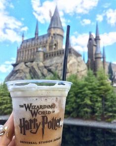 a person holding up a drink in front of hogwarts castle