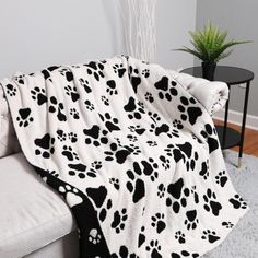 a black and white dog paw print blanket sitting on top of a couch next to a potted plant