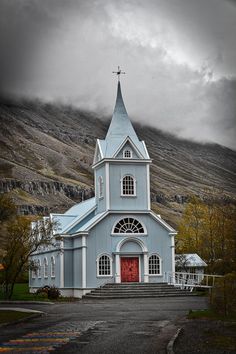 a blue church with a steeple and red door in front of a mountain range