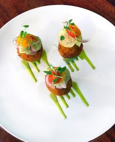 three small appetizers are on a white plate with green garnishes