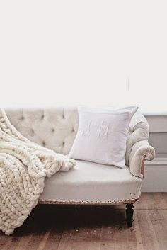 a white couch sitting in front of a window next to a blanket on top of it