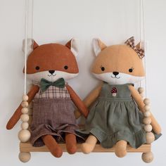 two stuffed animals are sitting on a wooden swing hanging from the wall, one is wearing a dress and the other has a bow tie