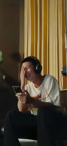 a young man sitting in front of a tv holding his headphones to his ear