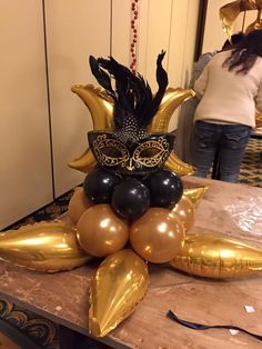 a table topped with balloons and an elaborate mask on top of it's head