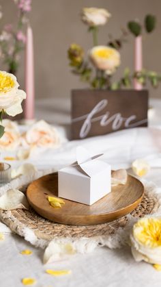 a small white box sitting on top of a wooden plate next to flowers and candles