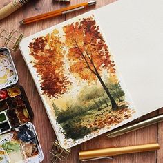 an artist's notebook with watercolors and paintbrushes next to it