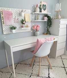 a white desk topped with a pink pillow next to a shelf filled with plants and flowers