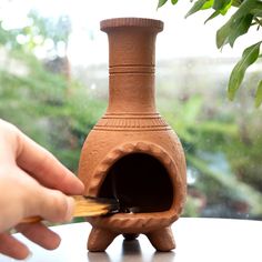 a person is holding a piece of wood near a clay pot with a hole in it