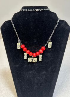 a necklace with dices and red beads on a black display stand in front of a white background