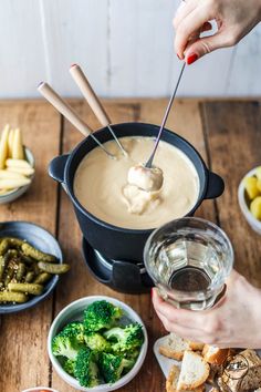 a person is dipping broccoli into some soup in a crock pot on a wooden table