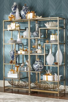 a gold shelf with blue and white vases on it in front of a wall