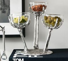 three glass goblets filled with olives, limes and nuts on top of a table