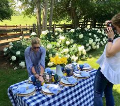 two women are standing at a table with plates and cups on it, while one woman is taking a photo