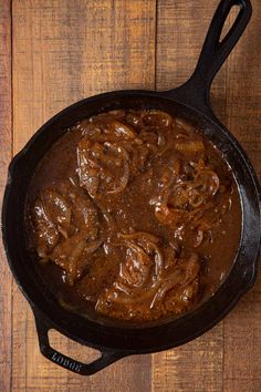 a skillet filled with meat and sauce on top of a wooden table