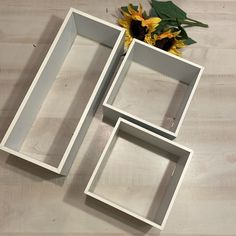 three empty white boxes sitting on top of a wooden table next to a sunflower