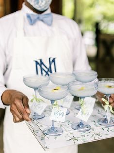 the waiter is holding several martini glasses with labels on them and place cards in front of them