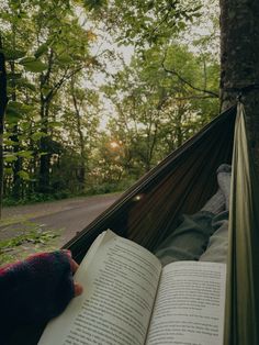 a person laying in a hammock reading a book and holding an open book