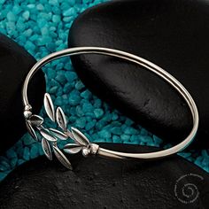 a silver bracelet sitting on top of a rock next to some rocks and blue pebbles